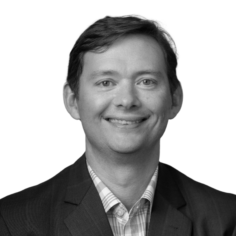Black and white professional headshot of Tom Rhoades, CFO of Provar, wearing a dark suit jacket and striped collared shirt, smiling against a black background.